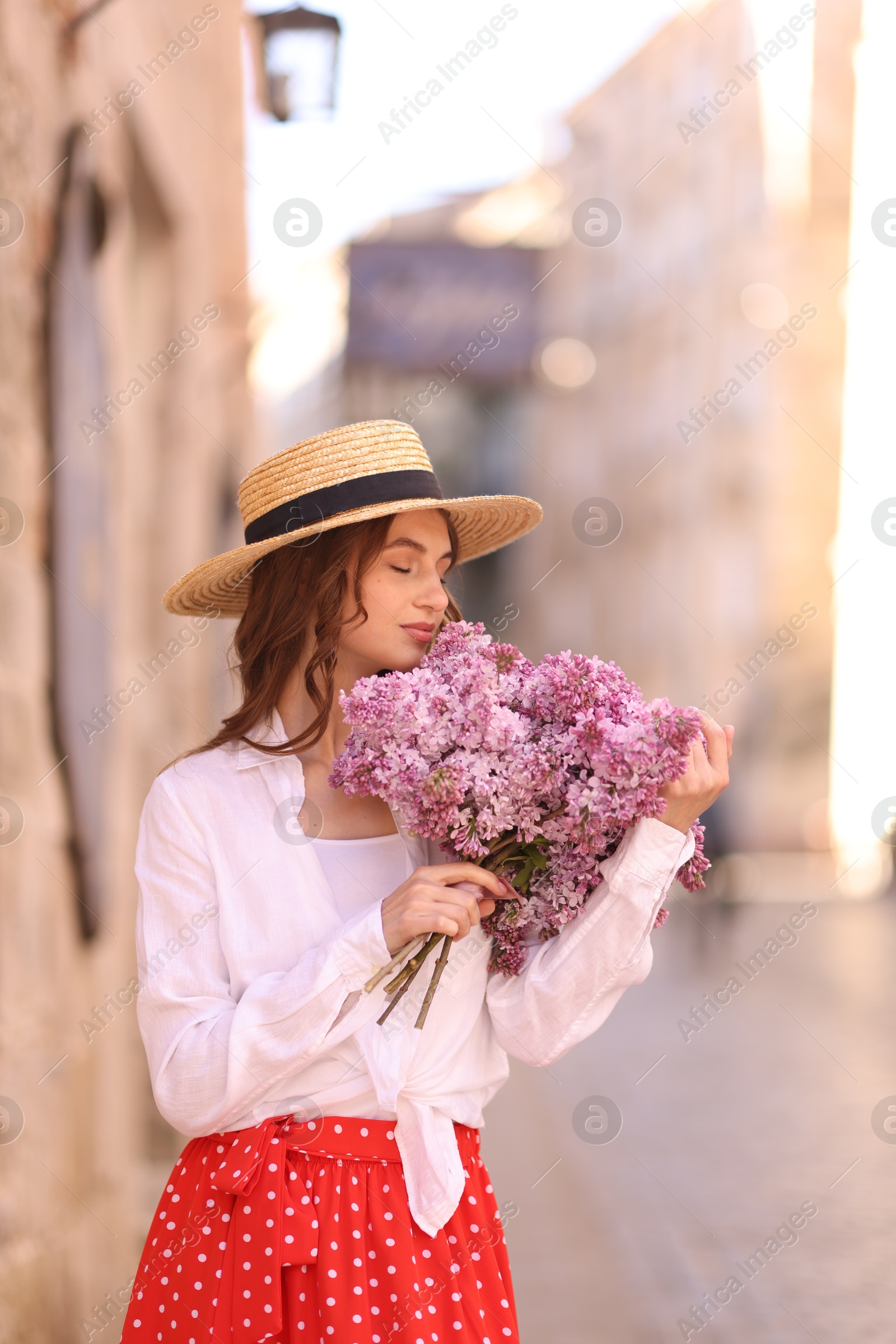 Beautiful woman in hat with bouquet of lilac flowers near building outdoors Photo of Beautiful woman in hat with bouquet of lilac flowers near building outdoors