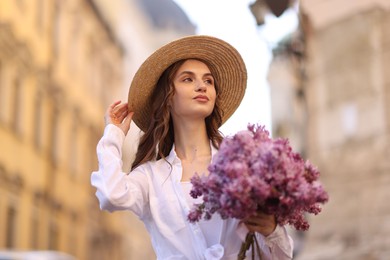 Photo of Beautiful woman in hat with bouquet of lilac flowers outdoors, low angle view