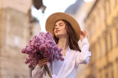 Photo of Beautiful woman in hat with bouquet of lilac flowers outdoors, low angle view