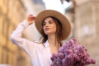 Photo of Beautiful woman in hat with bouquet of lilac flowers outdoors, low angle view