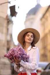 Photo of Beautiful woman in hat with bouquet of lilac flowers outdoors