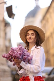 Photo of Smiling woman in hat with bouquet of lilac flowers outdoors