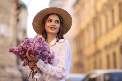 Photo of Smiling woman in hat with bouquet of lilac flowers outdoors. Space for text