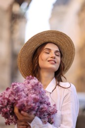 Photo of Smiling woman in hat with bouquet of lilac flowers outdoors