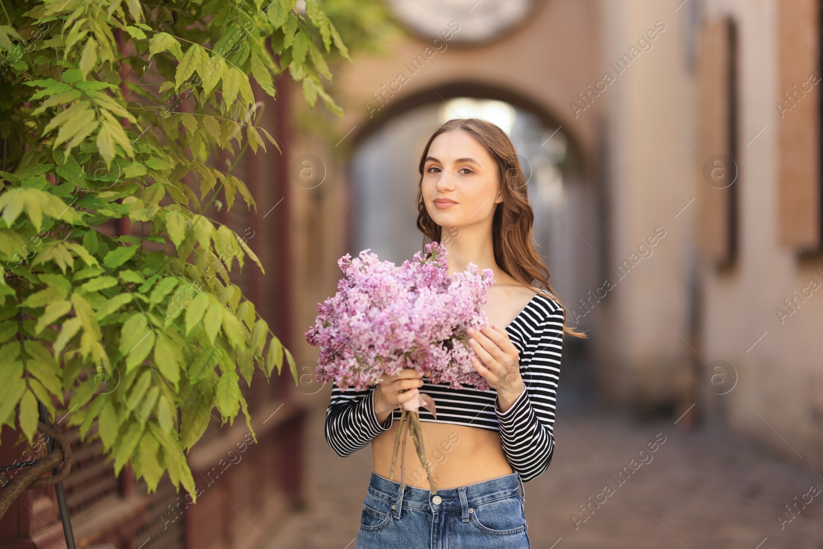 Beautiful woman with bouquet of lilac flowers near tree on city street Photo of Beautiful woman with bouquet of lilac flowers near tree on city street