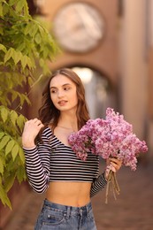 Photo of Beautiful woman with bouquet of lilac flowers near tree on city street