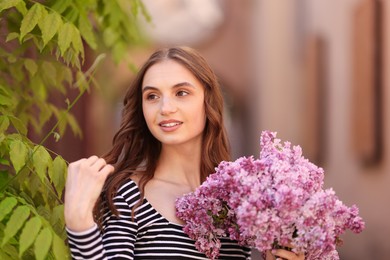 Photo of Smiling woman with bouquet of lilac flowers outdoors
