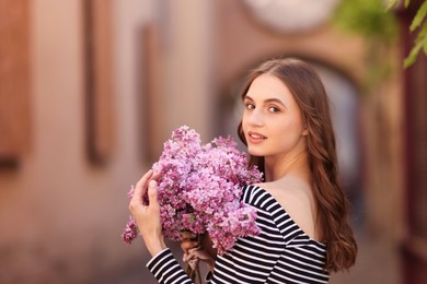 Photo of Beautiful woman with bouquet of lilac flowers outdoors. Space for text