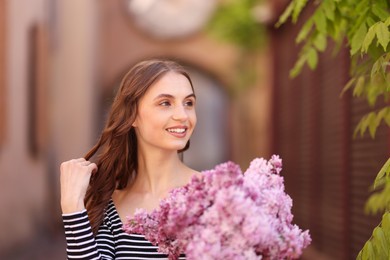Photo of Smiling woman with bouquet of lilac flowers outdoors