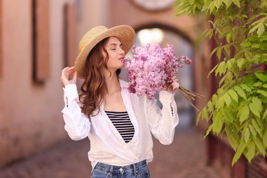 Photo of Beautiful woman with bouquet of lilac flowers near tree on city street