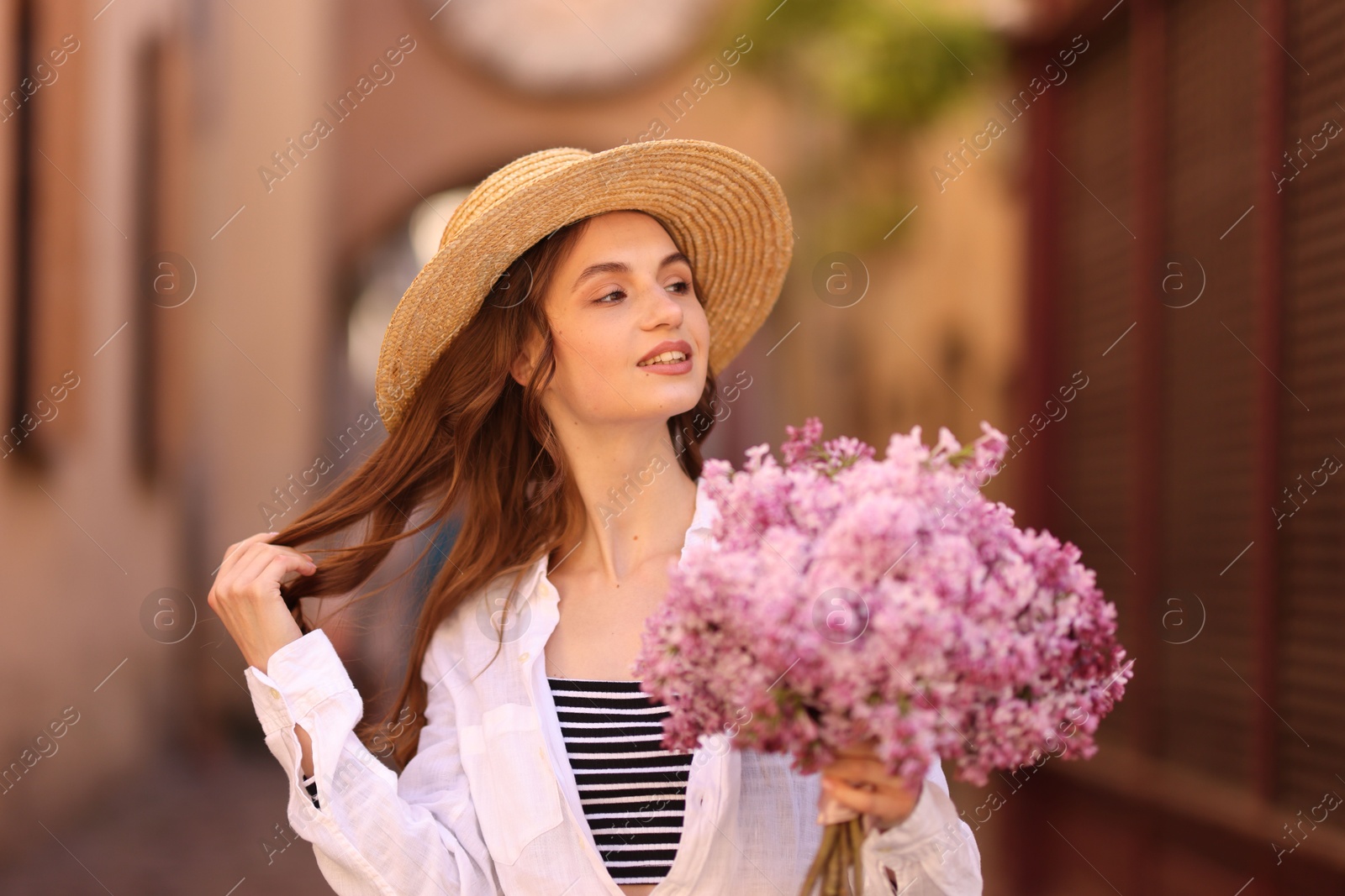 Smiling woman in hat with bouquet of lilac flowers on city street Photo of Smiling woman in hat with bouquet of lilac flowers on city street