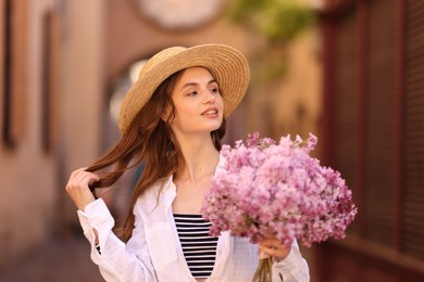 Photo of Smiling woman in hat with bouquet of lilac flowers on city street