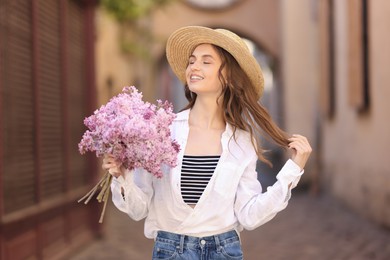 Photo of Smiling woman in hat with bouquet of lilac flowers on city street