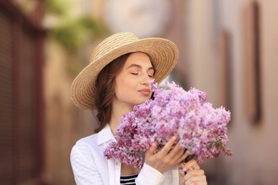 Photo of Beautiful woman in hat with bouquet of lilac flowers on blurred background
