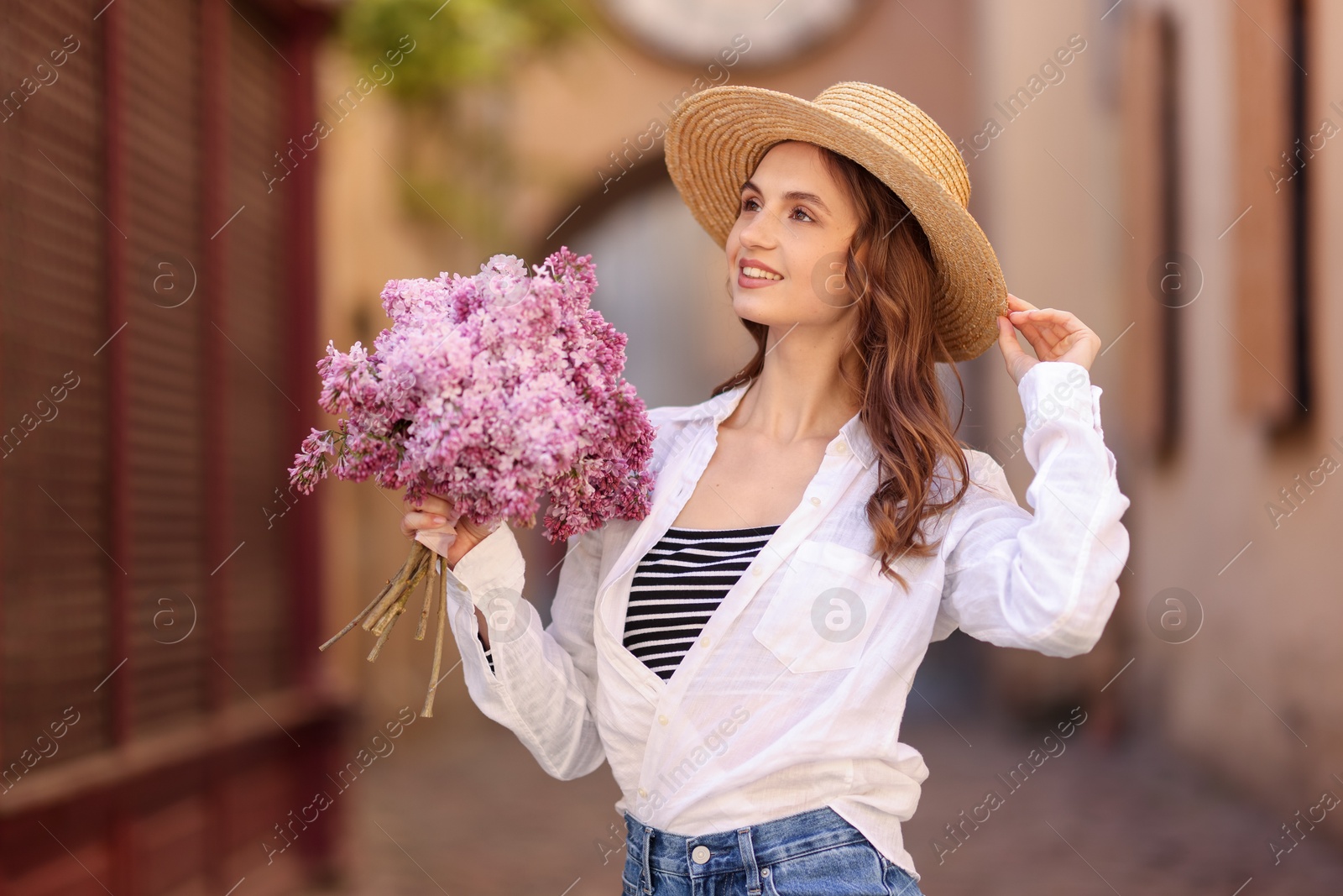 Smiling woman in hat with bouquet of lilac flowers on city street Photo of Smiling woman in hat with bouquet of lilac flowers on city street