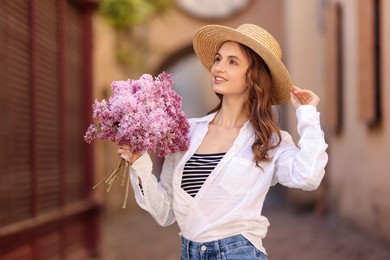 Photo of Smiling woman in hat with bouquet of lilac flowers on city street