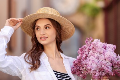 Photo of Smiling woman in hat with bouquet of lilac flowers on blurred background, closeup
