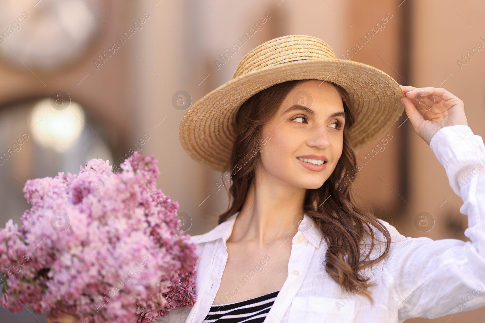 Smiling woman in hat with bouquet of lilac flowers on blurred background, closeup Photo of Smiling woman in hat with bouquet of lilac flowers on blurred background, closeup