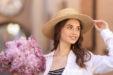 Photo of Smiling woman in hat with bouquet of lilac flowers on blurred background, closeup