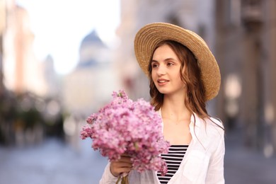 Photo of Smiling woman in hat with bouquet of lilac flowers on blurred background. Space for text