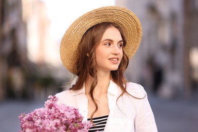 Photo of Smiling woman in hat with bouquet of lilac flowers on blurred background