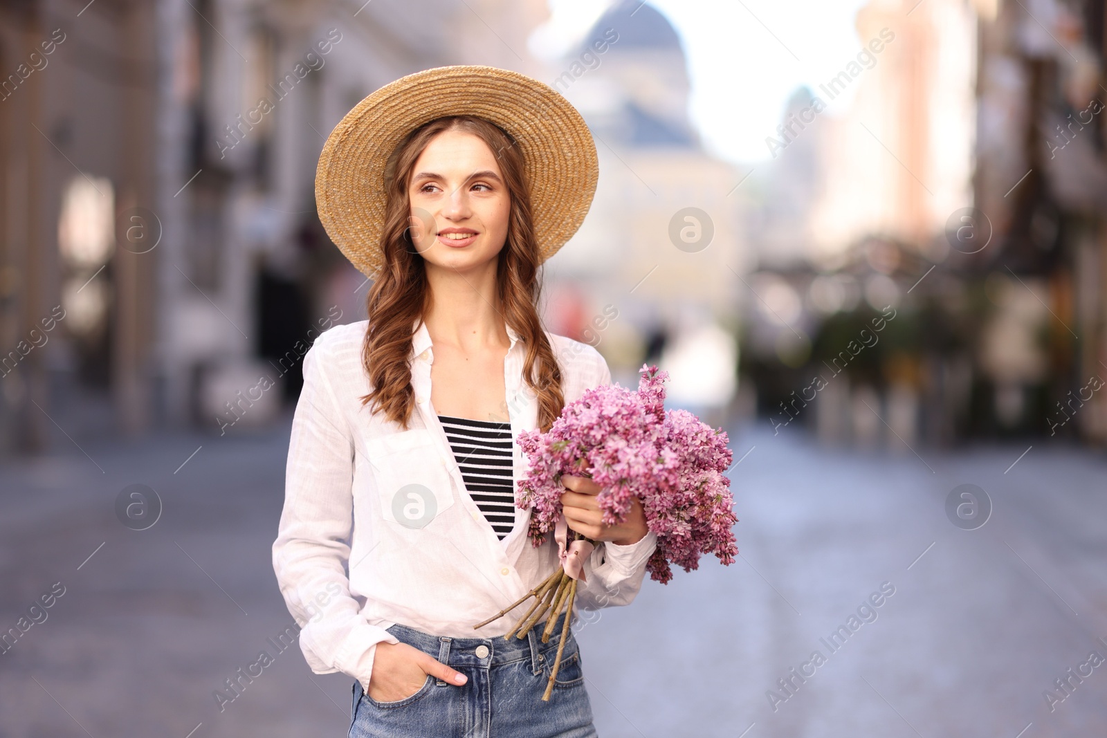 Smiling woman in hat with bouquet of lilac flowers on city street Photo of Smiling woman in hat with bouquet of lilac flowers on city street