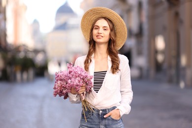 Photo of Smiling woman in hat with bouquet of lilac flowers on city street