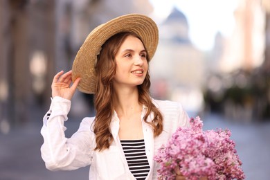 Photo of Smiling woman in hat with bouquet of lilac flowers on blurred background