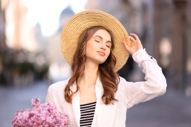 Photo of Beautiful woman in hat with bouquet of lilac flowers on blurred background