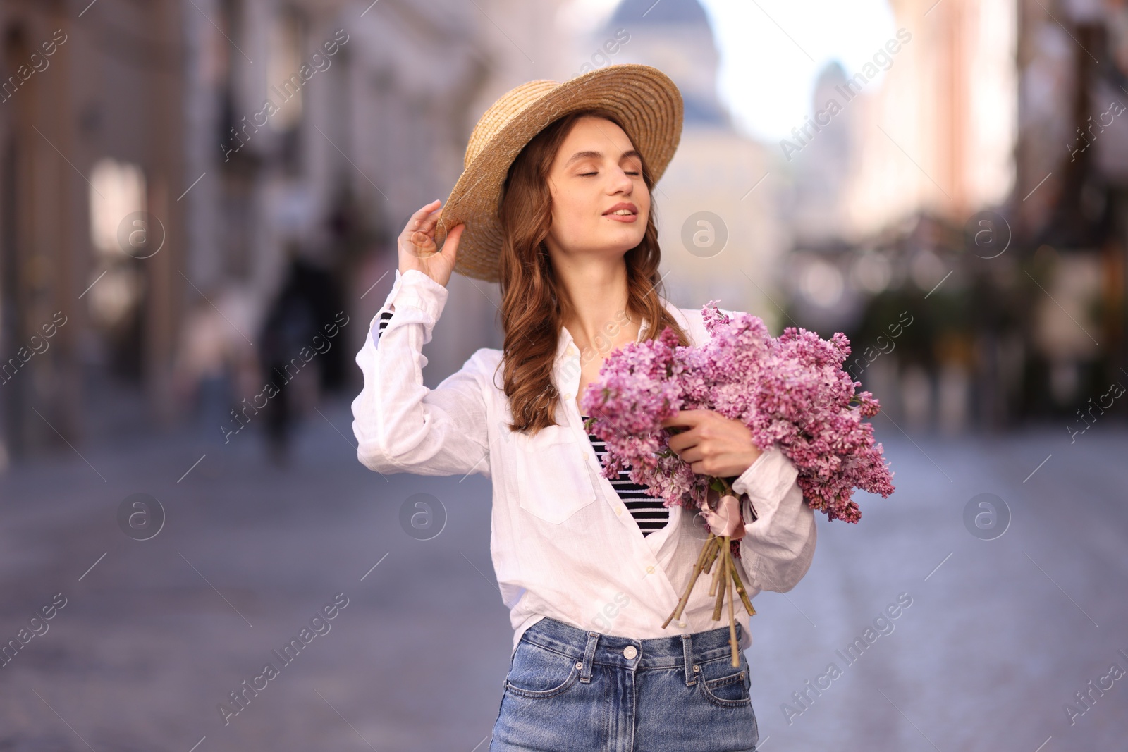 Smiling woman in hat with bouquet of lilac flowers on city street Photo of Smiling woman in hat with bouquet of lilac flowers on city street