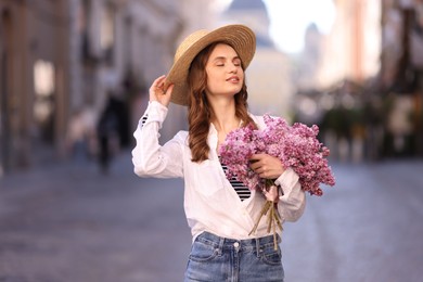 Photo of Smiling woman in hat with bouquet of lilac flowers on city street