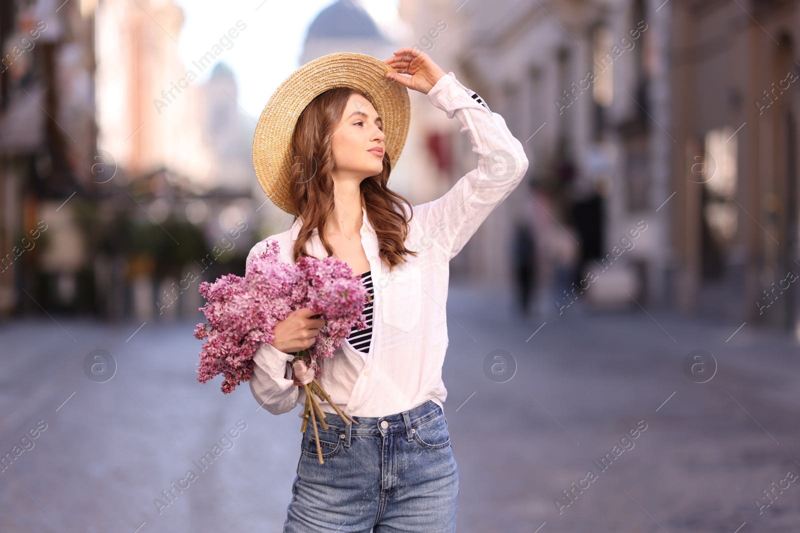 Beautiful woman in hat with bouquet of lilac flowers on city street Photo of Beautiful woman in hat with bouquet of lilac flowers on city street