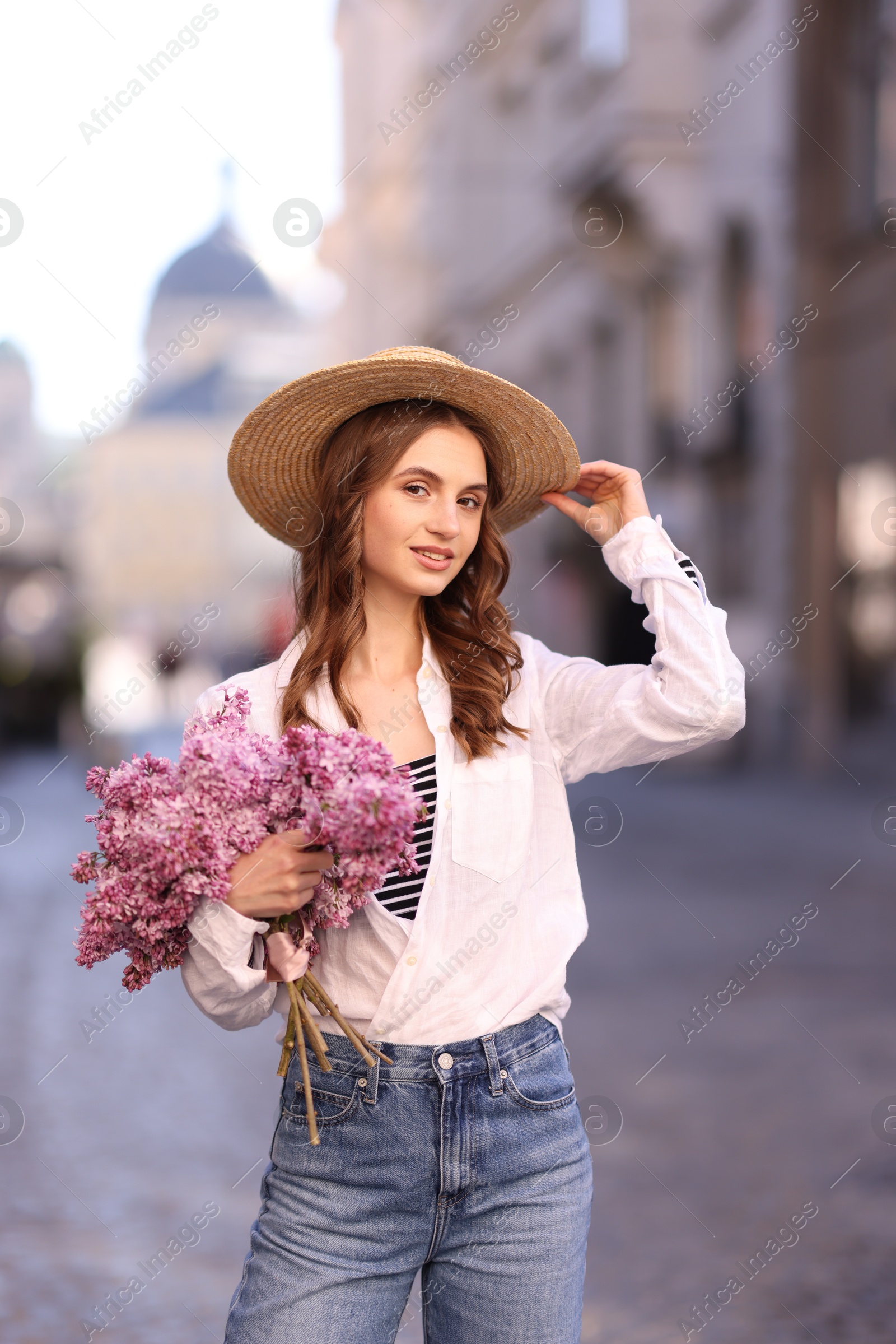 Smiling woman in hat with bouquet of lilac flowers on city street Photo of Smiling woman in hat with bouquet of lilac flowers on city street