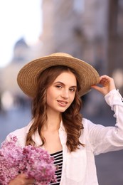 Photo of Smiling woman in hat with bouquet of lilac flowers on blurred background