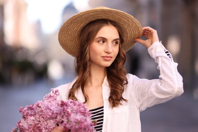 Photo of Beautiful woman in hat with bouquet of lilac flowers on blurred background