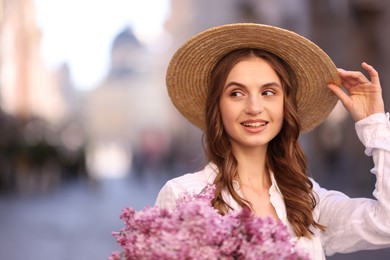 Photo of Smiling woman in hat with bouquet of lilac flowers on blurred background. Space for text