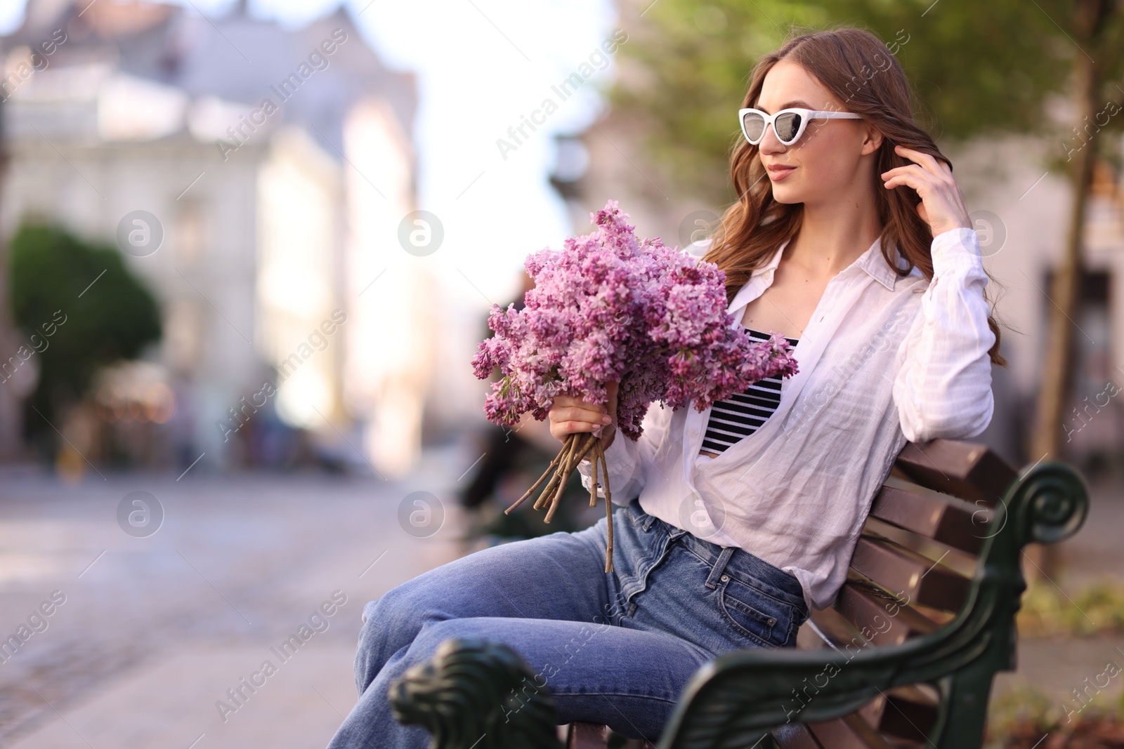 Beautiful woman in sunglasses with bouquet of lilac flowers sitting on bench outdoors. Space for text Photo of Beautiful woman in sunglasses with bouquet of lilac flowers sitting on bench outdoors. Space for text