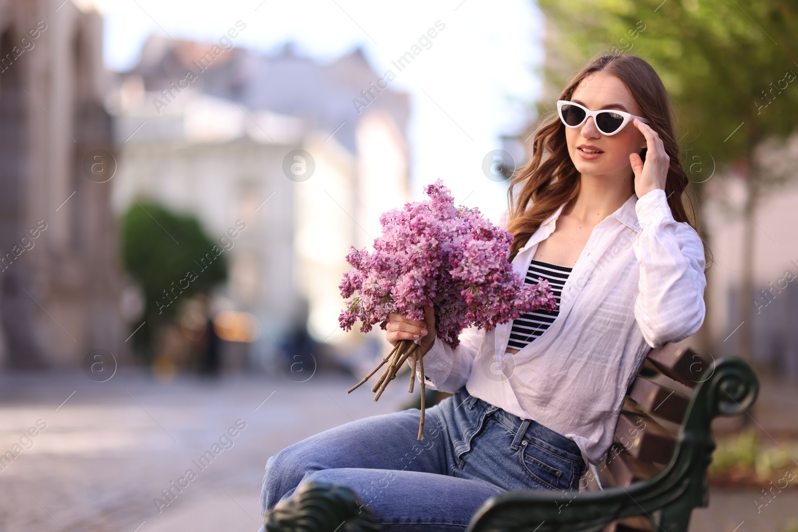 Beautiful woman in sunglasses with bouquet of lilac flowers sitting on bench outdoors. Space for text Photo of Beautiful woman in sunglasses with bouquet of lilac flowers sitting on bench outdoors. Space for text