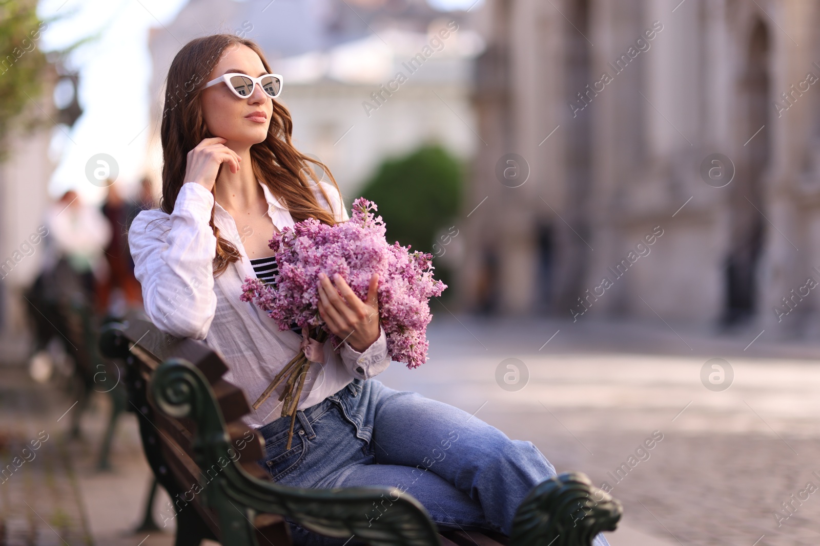 Beautiful woman in sunglasses with bouquet of lilac flowers sitting on bench outdoors. Space for text Photo of Beautiful woman in sunglasses with bouquet of lilac flowers sitting on bench outdoors. Space for text