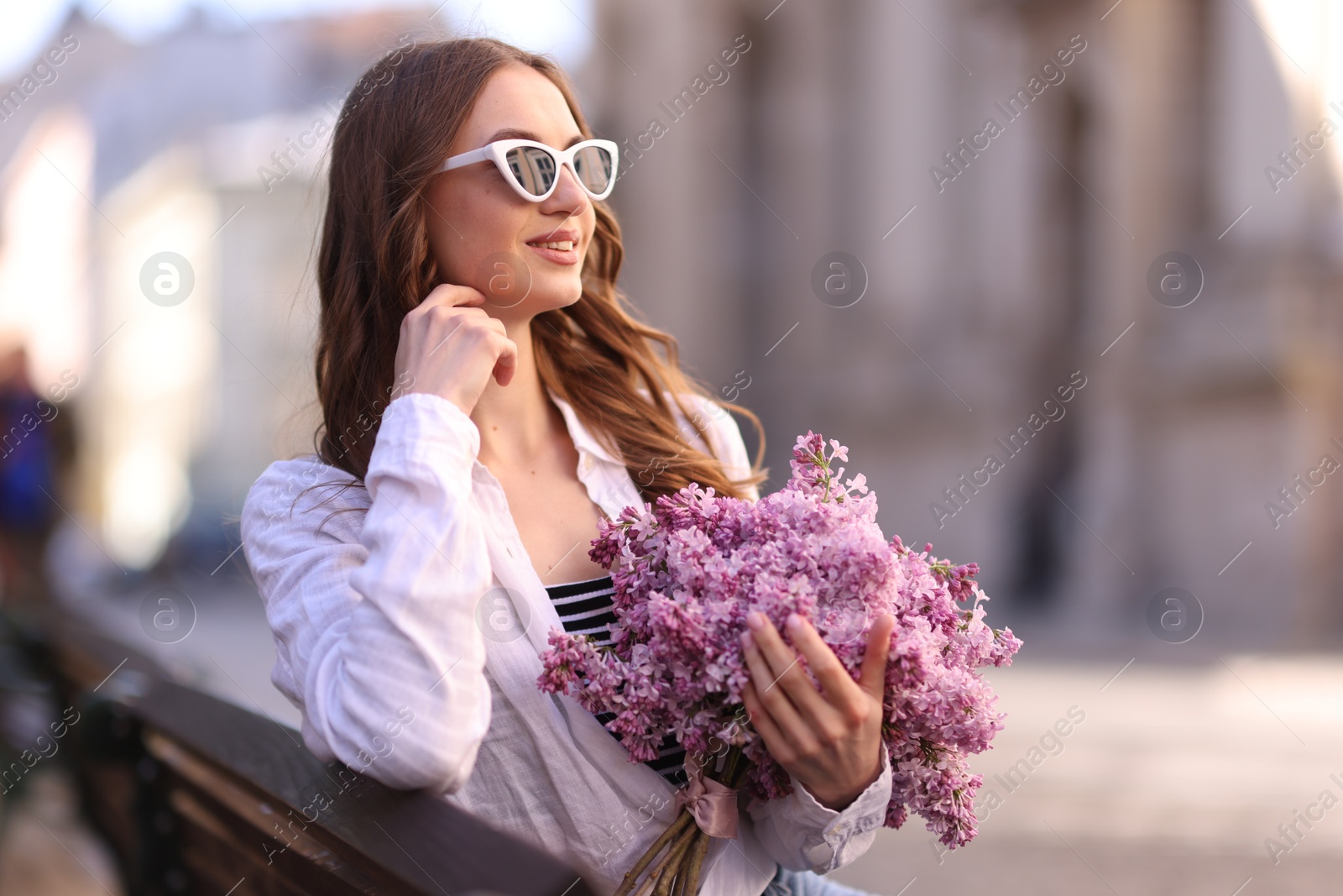 Beautiful woman in sunglasses with bouquet of lilac flowers on bench outdoors Photo of Beautiful woman in sunglasses with bouquet of lilac flowers on bench outdoors