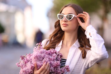 Photo of Beautiful woman in sunglasses with bouquet of lilac flowers outdoors