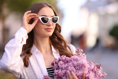 Photo of Beautiful woman in sunglasses with bouquet of lilac flowers outdoors