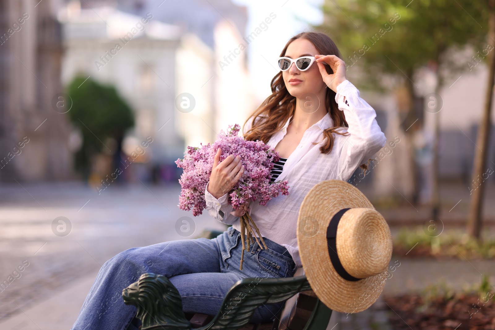 Beautiful woman in sunglasses with bouquet of lilac flowers sitting on bench outdoors Photo of Beautiful woman in sunglasses with bouquet of lilac flowers sitting on bench outdoors