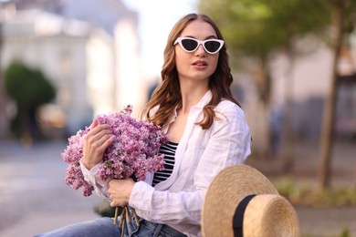 Photo of Beautiful woman in sunglasses with bouquet of lilac flowers outdoors