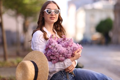 Photo of Beautiful woman in sunglasses with bouquet of lilac flowers outdoors