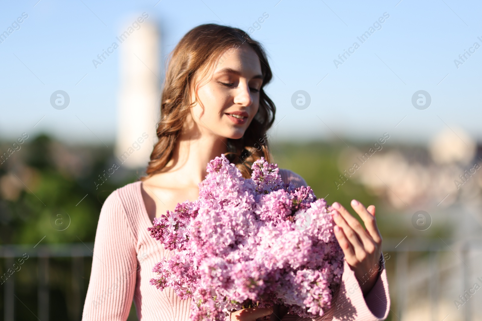 Smiling woman with bouquet of lilac flowers outdoors in morning Photo of Smiling woman with bouquet of lilac flowers outdoors in morning