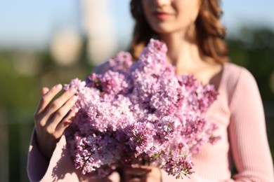 Photo of Woman with bouquet of lilac flowers outdoors in morning, selective focus