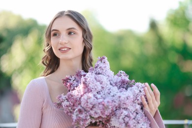 Photo of Smiling woman with bouquet of lilac flowers outdoors in morning