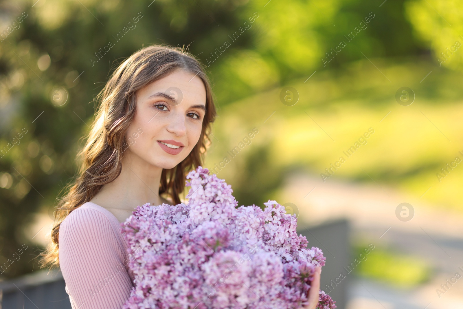 Smiling woman with bouquet of lilac flowers outdoors in morning. Space for text Photo of Smiling woman with bouquet of lilac flowers outdoors in morning. Space for text