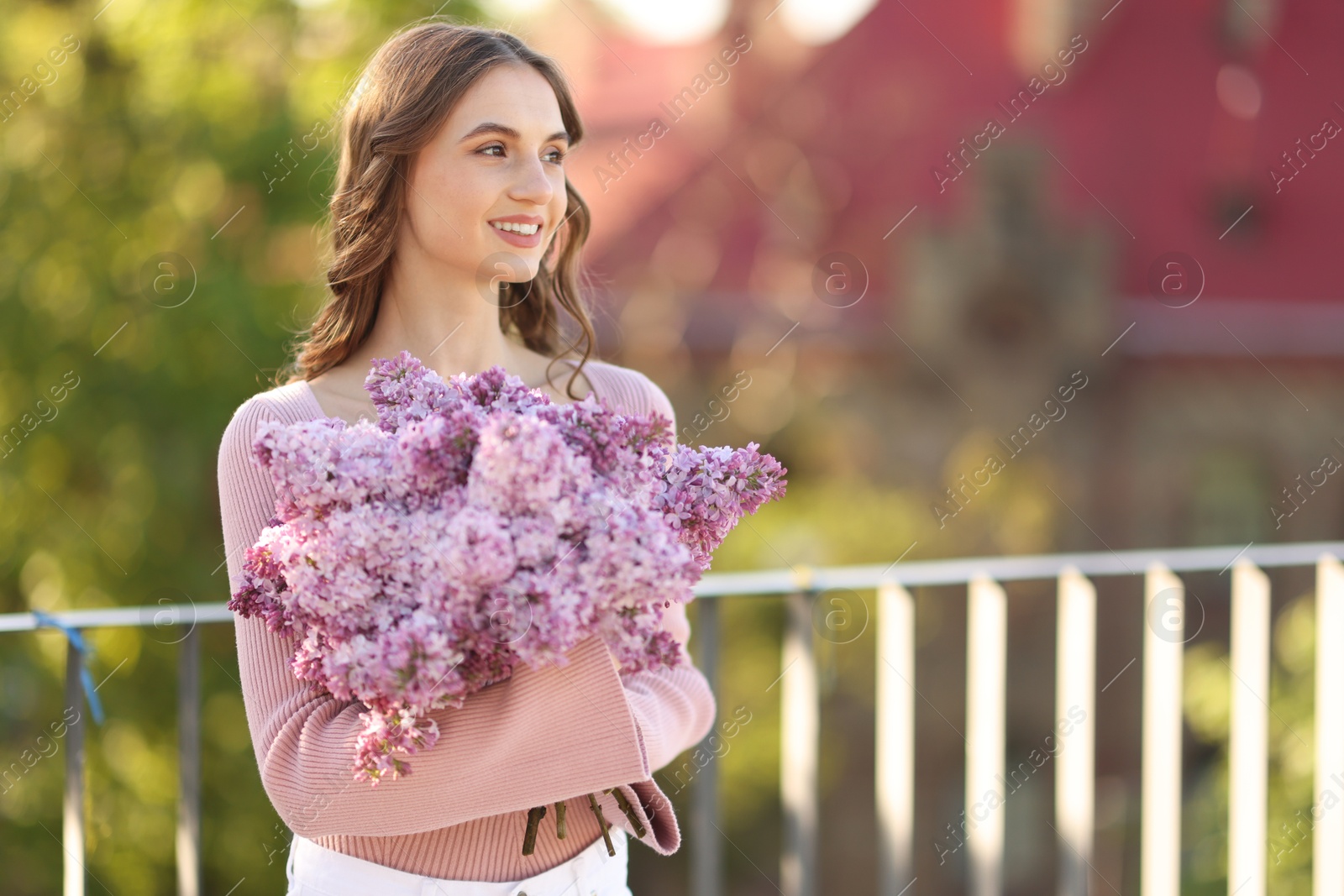 Smiling woman with bouquet of lilac flowers outdoors in morning. Space for text Photo of Smiling woman with bouquet of lilac flowers outdoors in morning. Space for text